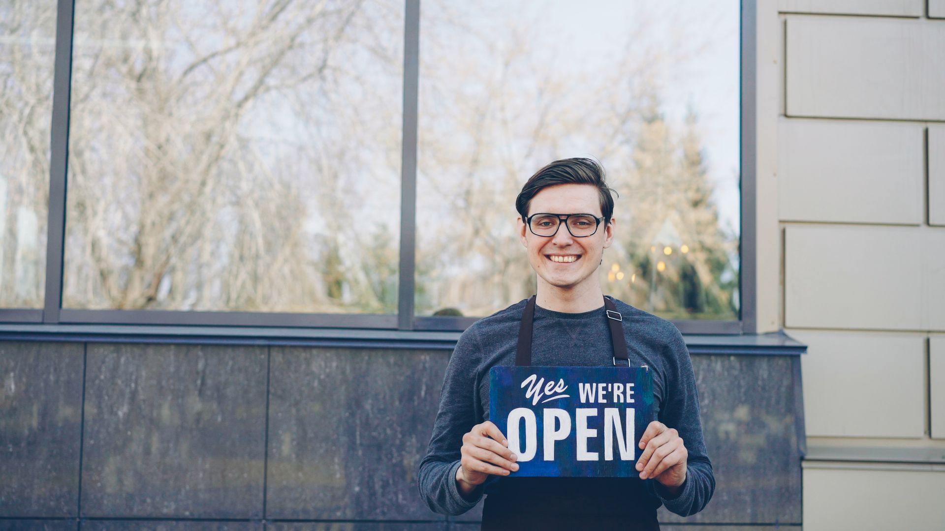 Elinde "Yes We're Open" tabelası tutan gülümseyen işletme sahibi
